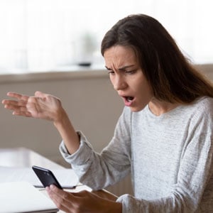  Surprised woman holds cell phone, potentially learning about dischargeable debts - THE LAW OFFICES OF DIANE ANDERSON